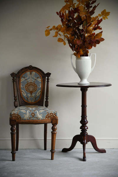 An antique chair with tapestry upholstery next to an antique side table.