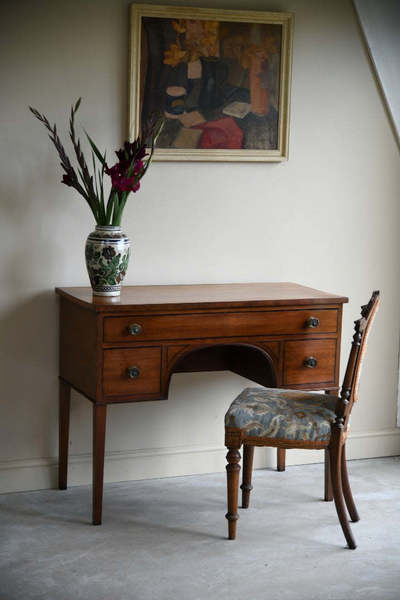 An antique mahogany desk and chair against a pale wall.