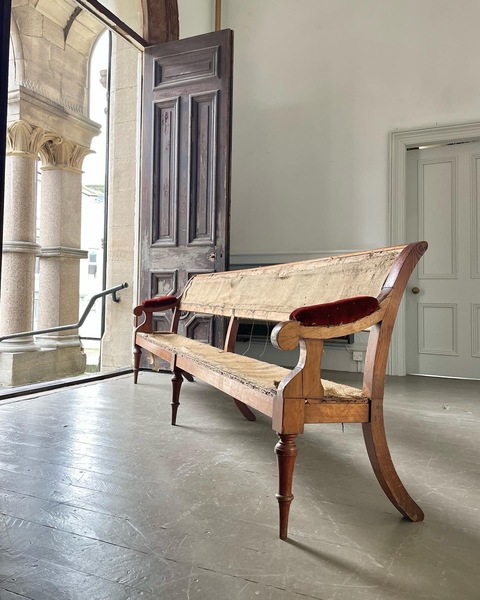 Late Regency-era hall bench, looking out towards grand corinthian columns through a double doorway.