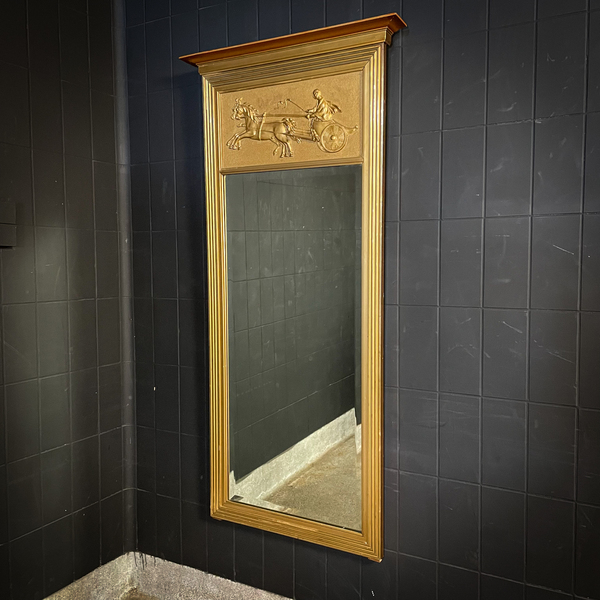 A gold Eglomise mirror hanging on a black brick wall.