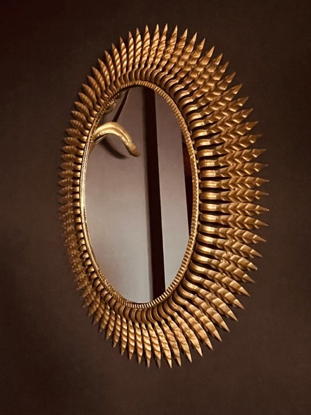 A gold sunburst-style mirror hung in a black wall.