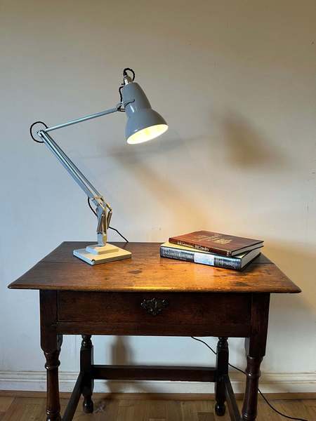 A grey Anglepoise light illuminating a book on an antique table.