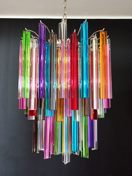A multicolour glass chandelier in front of a black wall.