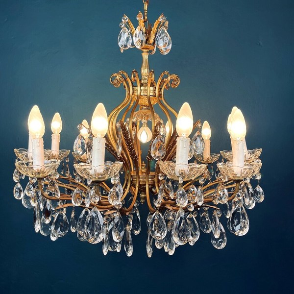 A Hollywood Regency chandelier with cut-glass tear drops adornments against a teal-coloured wall.