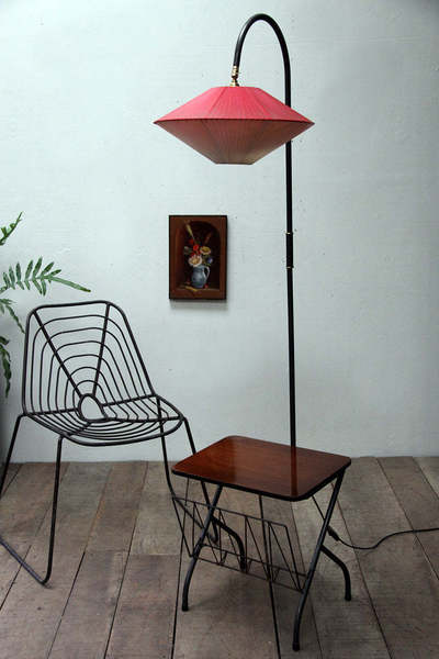 A floor lamp with a red satellite-shaped lampshade next to a wire chair.