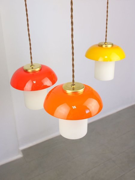 Three mushroom-shaped pendant lights in orange, red and yellow, hanging from a ceiling.