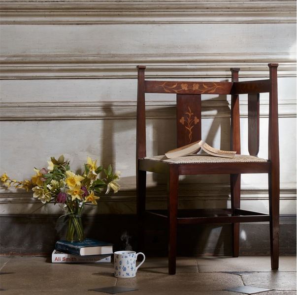 An arts and crafts corner chair with a book resting open on the seat and positioned next to a vase of flowers