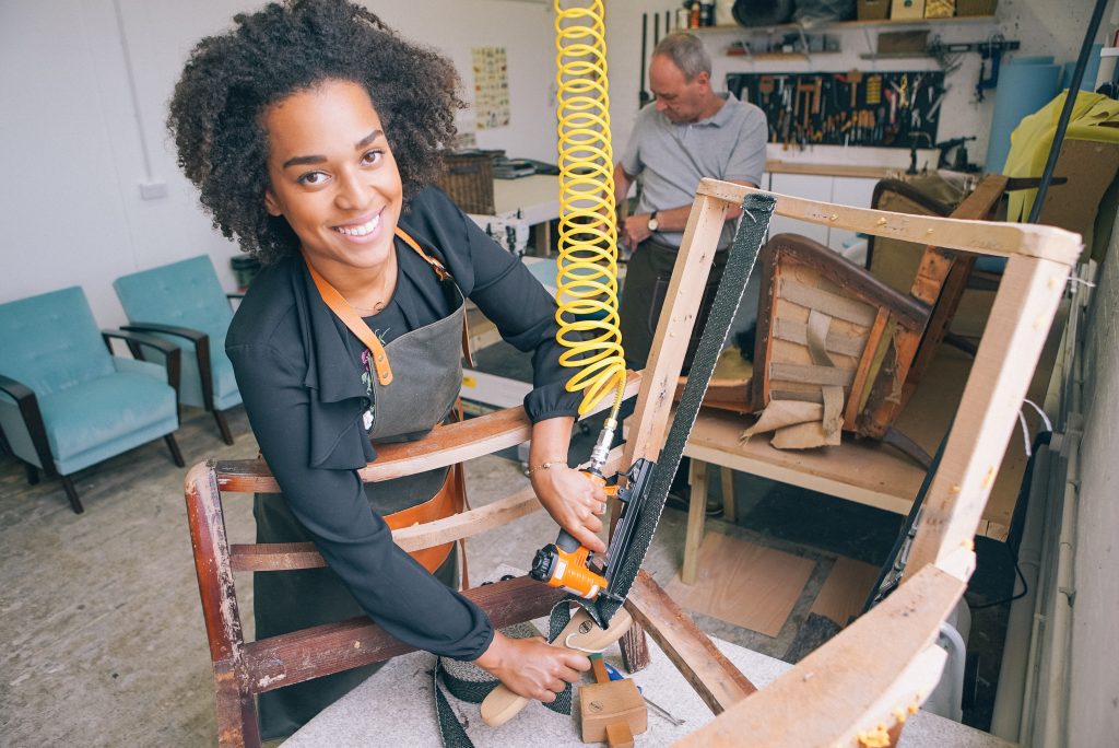 A woman posing while reupholstering a chair.