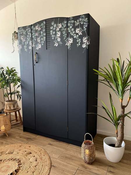 A wardrobe decorated in dark blue with a crown of falling flowers painted at the top.